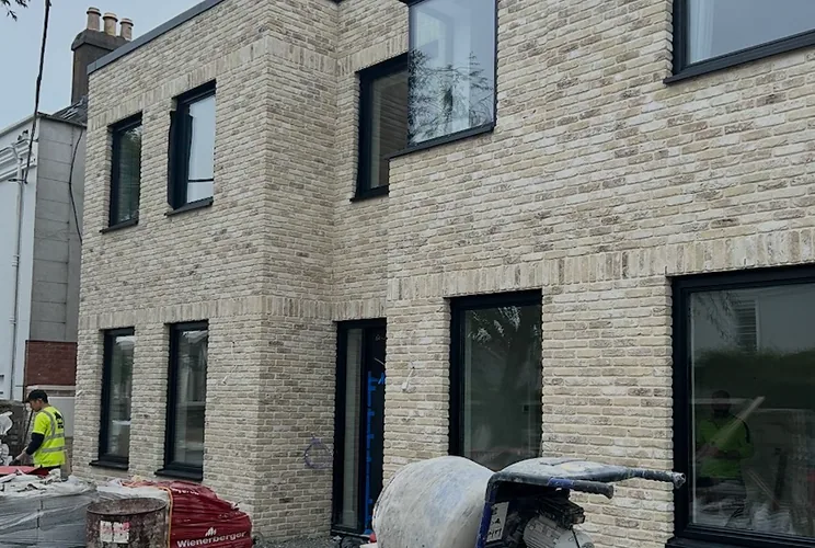 Two-storey buff brick house with black framed windows, under construction