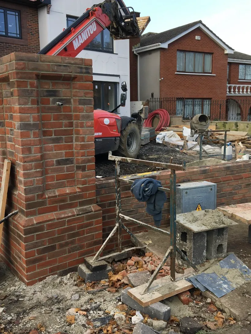 Red brick pier and low boundary wall under construction with a telehandler behind