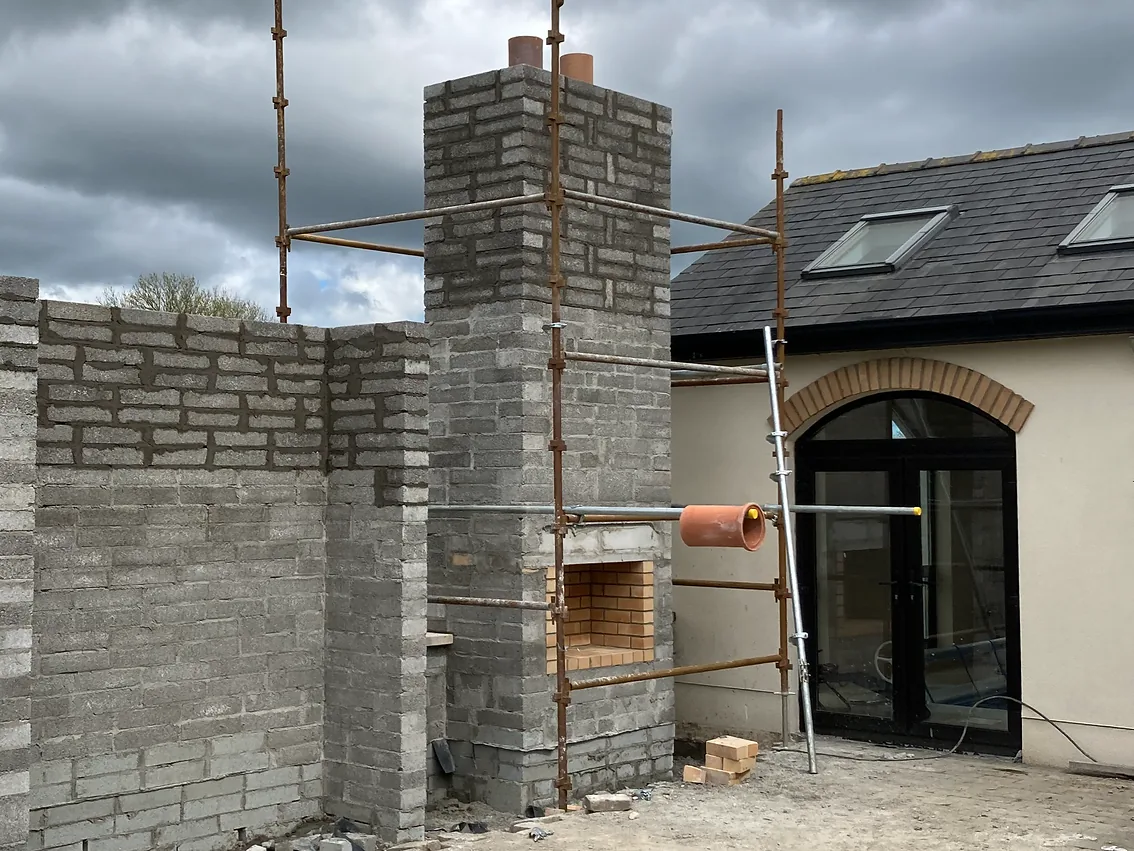 Rebuilt chimney stack in grey block, seen from scaffolding against a cloudy sky
