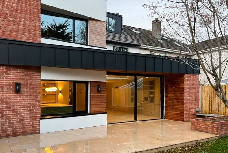 Two-storey rear extension in red brick with black zinc banding, timber cladding and travertine paving