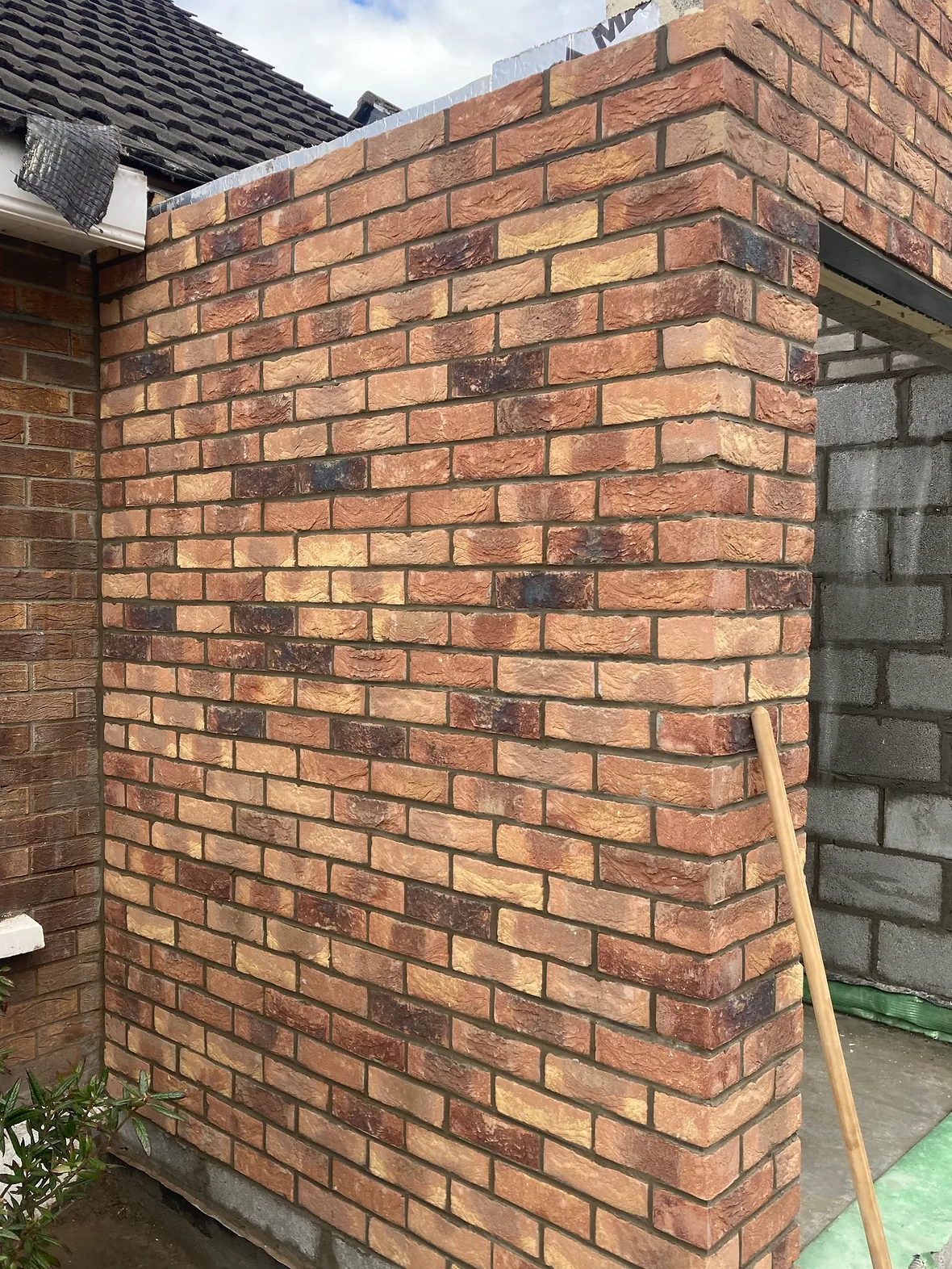 New multi red brick return meeting an older brick wall at a corner, blockwork visible to the right