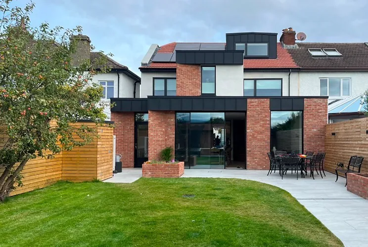 Rear extension and dormer in red brick with black zinc fascia, lawn and patio in front